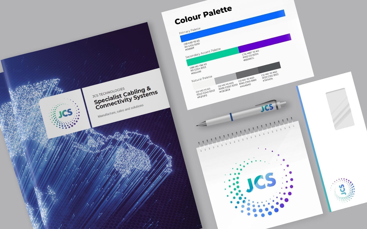 Marketing materials for JCS Technologies, including a brochure, color palette card, pen, notepad, and envelope, all branded with the JCS logo and colors.
