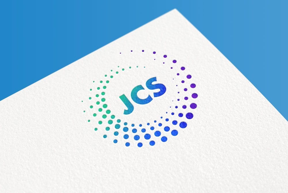 A logo featuring "JCS" at the center of a circular design made of colored dots, elegantly displayed on white paper. The background is a vibrant blue.