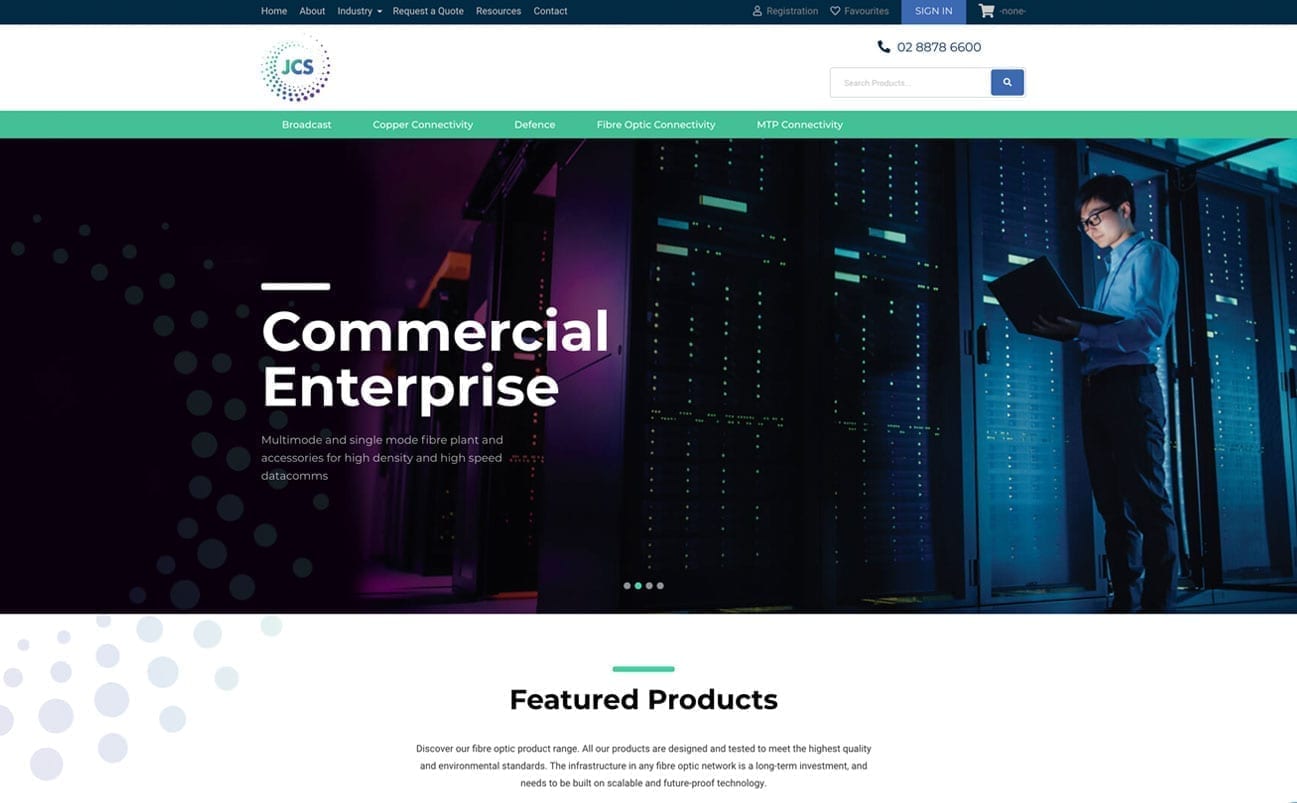 A man stands with a laptop in a server room on a webpage displaying JCS. The webpage highlights products and services related to commercial enterprise connectivity.