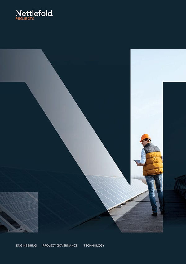 An engineer in a hard hat and vest reviews plans next to large solar panels with the logo and text "Nettlefold Projects" at the top.