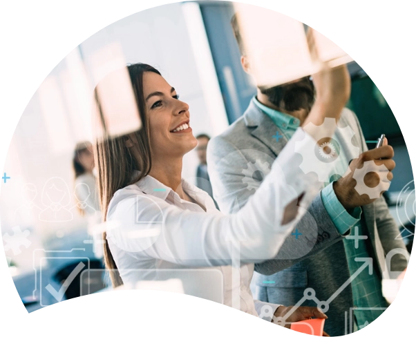A woman and a man in business attire are collaborating and writing on a glass board filled with various icons and symbols. The woman, representing their marketing agency, is smiling and focused on the board, strategizing their next digital marketing campaign.
