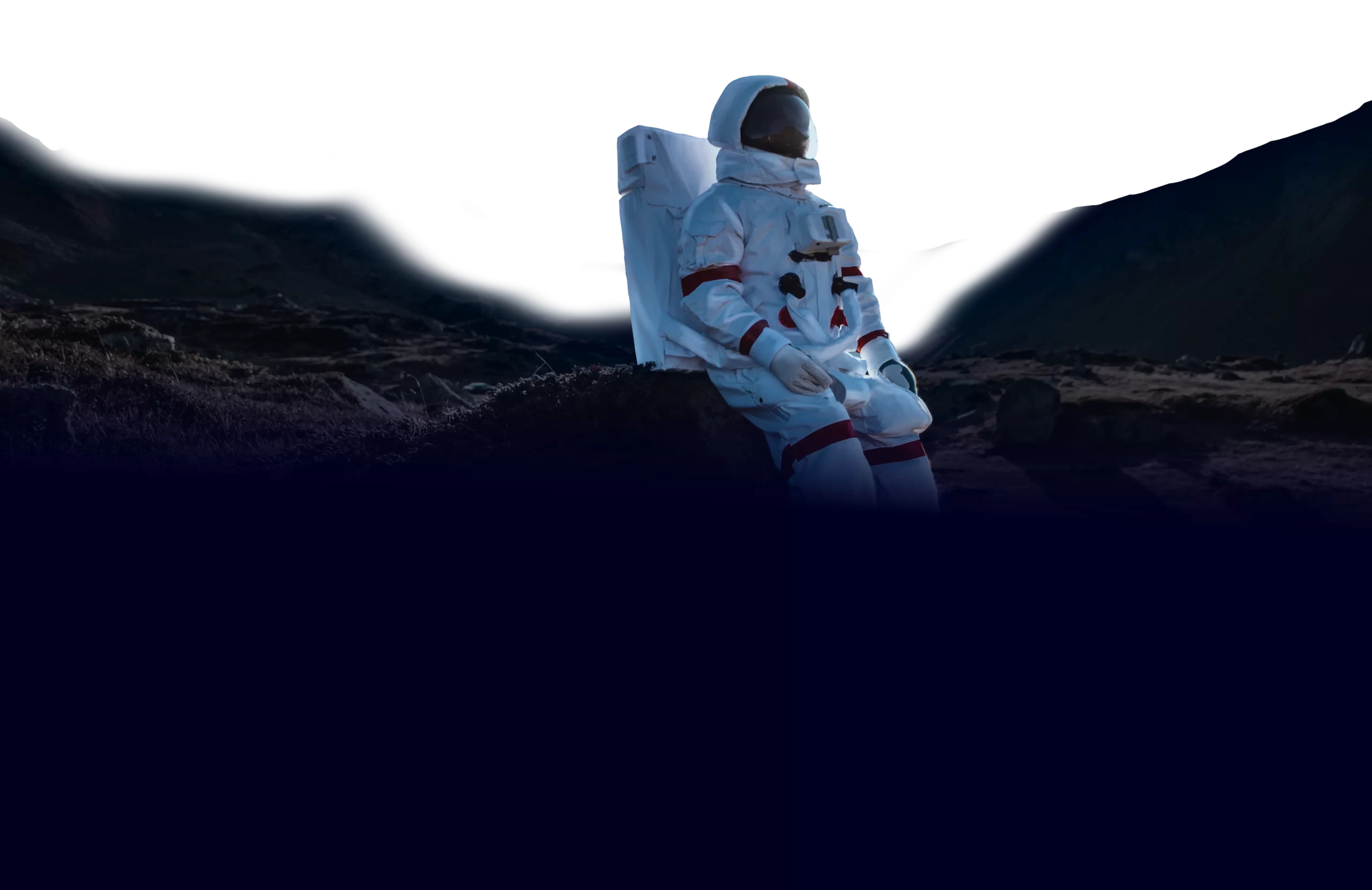 An astronaut wearing a white spacesuit sits on the surface of a dark, rocky terrain with a pitch-black sky in the background.